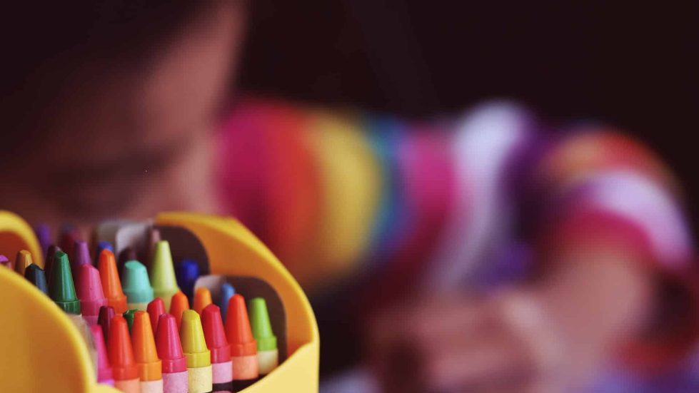 A box of crayons with a blurry background image of a child colouring