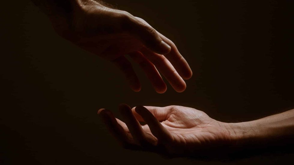 two hands about to meet amidst a shadowy background