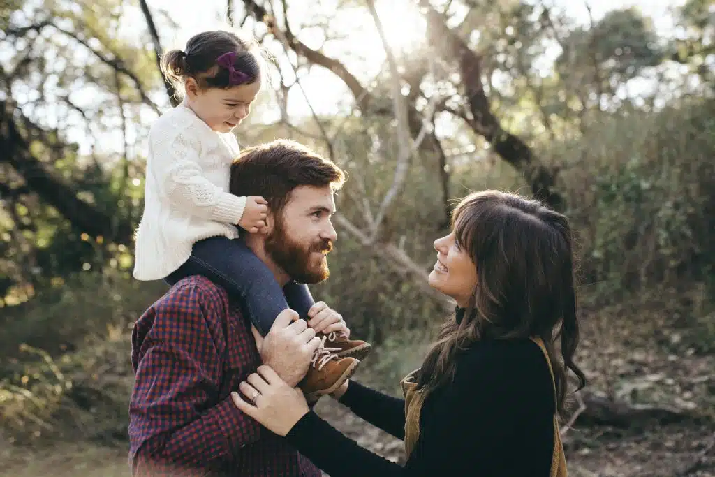 Chelsea gazes at her child who's sat atop her husbands shoulders
