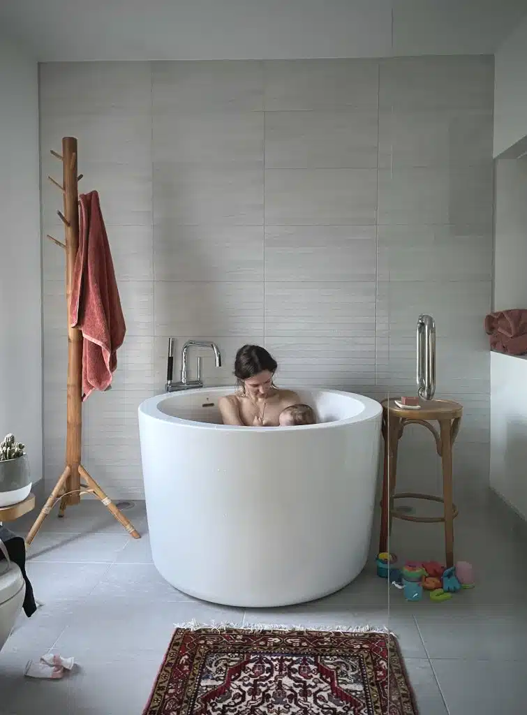Hillary sits in bathtub holding baby