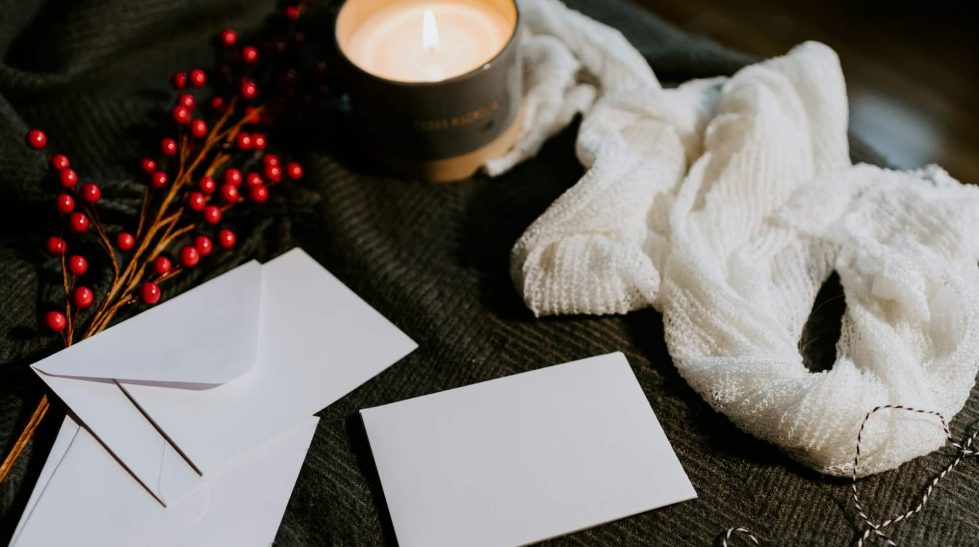 Christmas holly and envelopes on table with candle